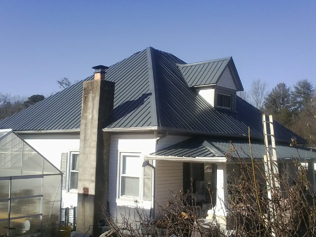 Dark blue standing seam metal roof on a white farmhouse with dormer — Slate & Tile Roof Repair by Roofing Brothers in Levittown