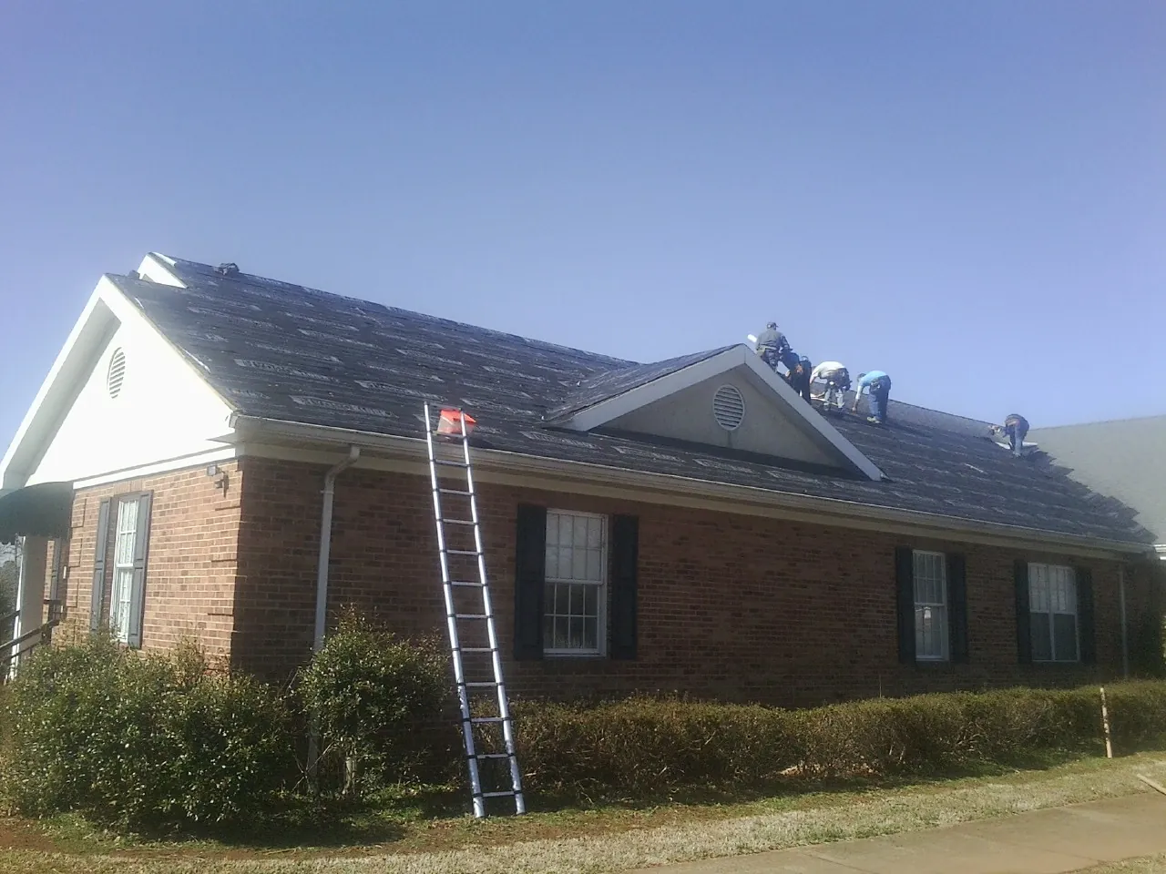 Crew tearing shingles off a brick ranch roof with a ladder set — Metal Roof Repair work by our crew in Levittown