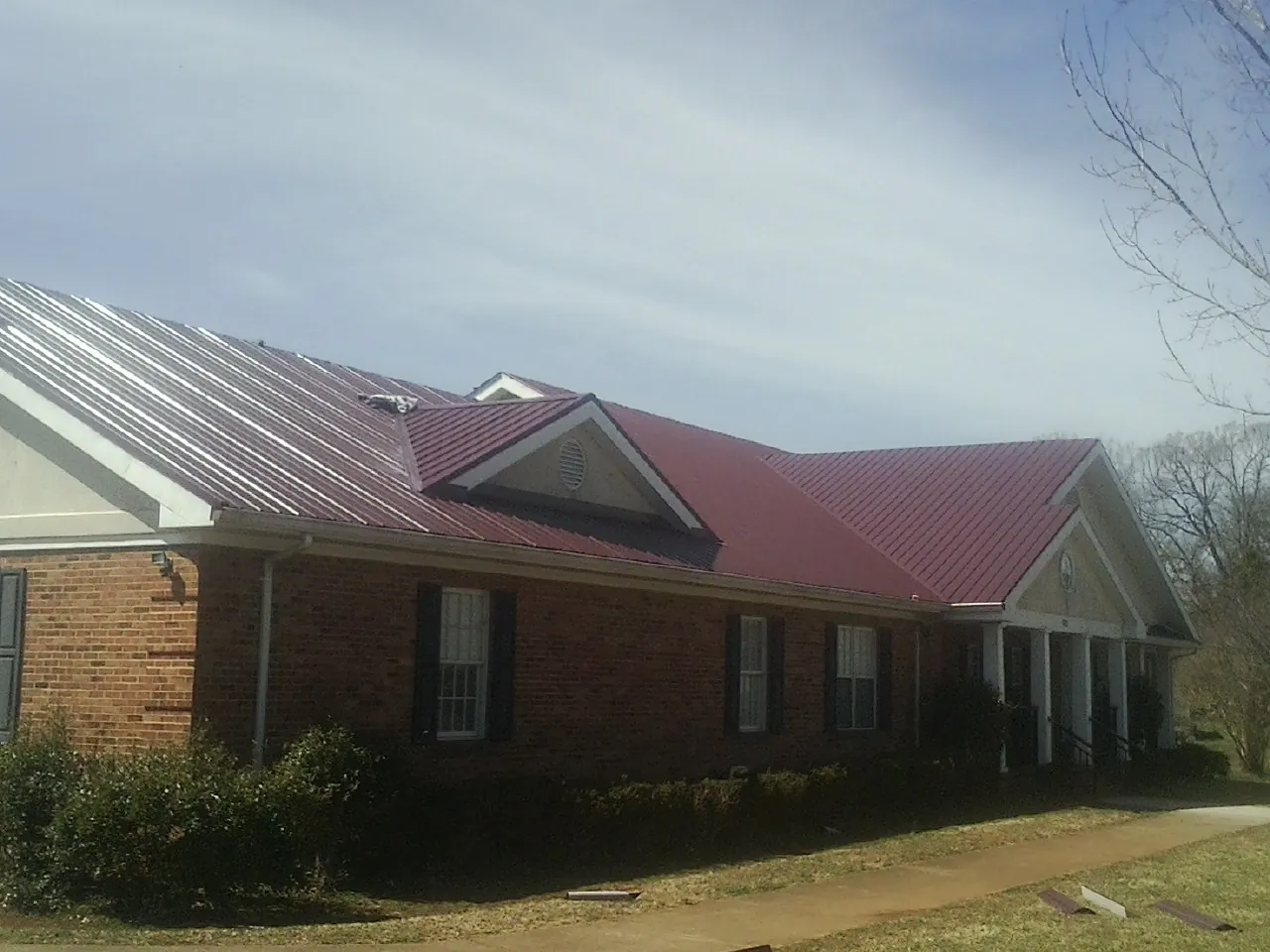 Red metal roof with gabled entries on a long brick building, from a Hail Damage Roof Repair job in Levittown