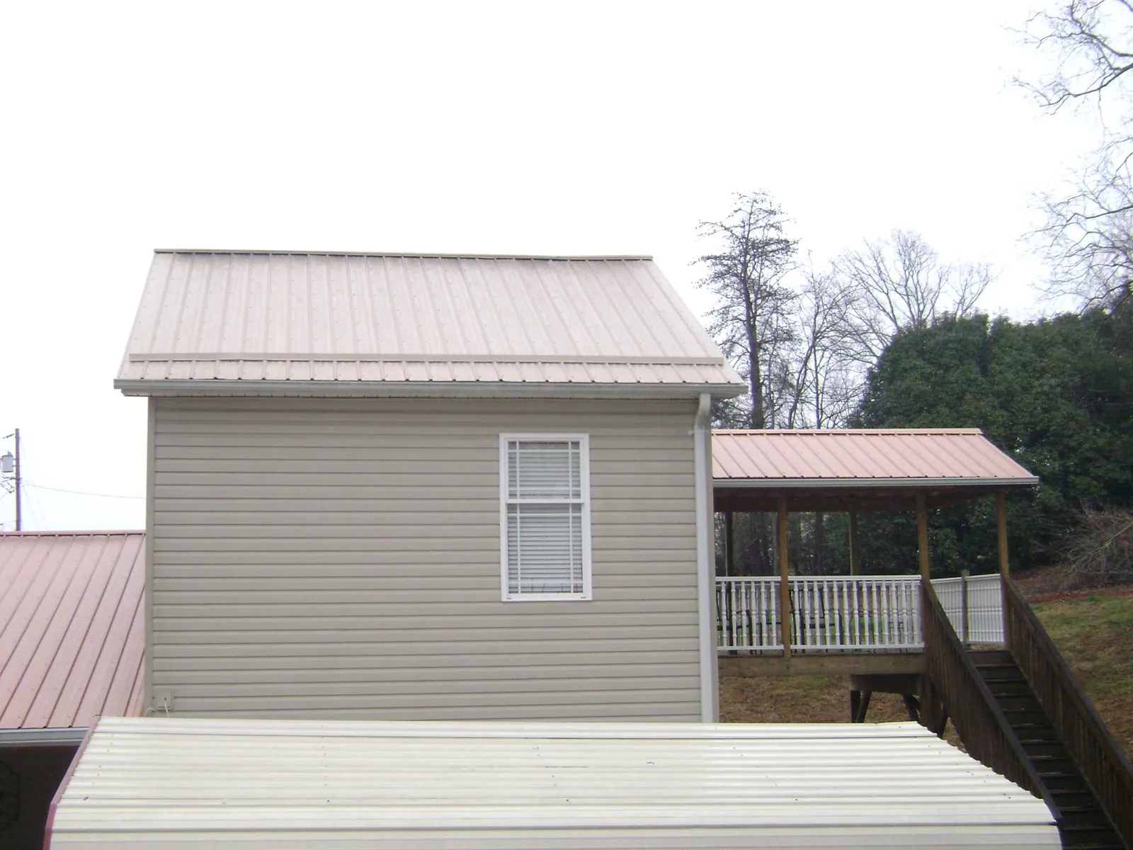 Tan metal roofs on a two story addition and attached porch, from a Roof Replacement job in Levittown